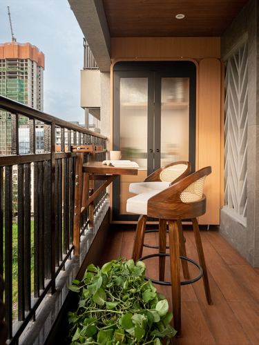 Compact balcony with cane bar stools, fold-down table, and fluted wood cabinet against city view