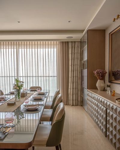Dining room with long table, sheer curtains, and textured sideboard beside window