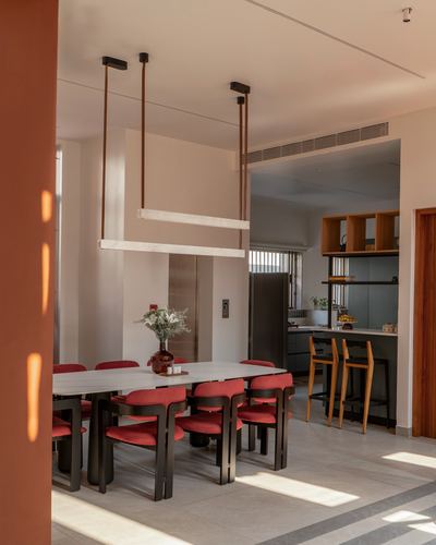 Sunlit dining room with red chairs, long stone table, and suspended linear pendant light