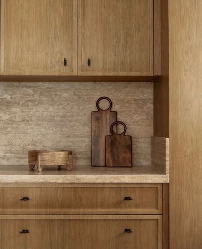 Close-up of wood kitchen cabinetry with stone backsplash and two wooden cutting boards on counter