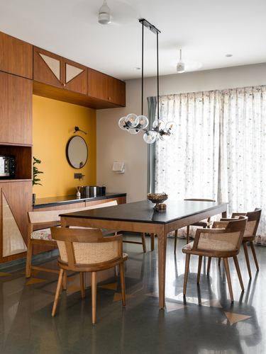 Dining area with black-top wood table, cane chairs, and multi-globe pendant lights against a mustard wall