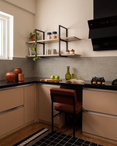 L-shaped kitchen with black countertop, pale cabinetry, open shelves and a leather chair at a nook
