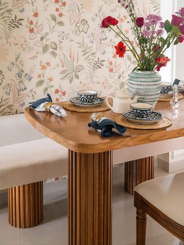 Fluted wood dining table set with blue floral crockery against floral wallpaper and fresh flowers