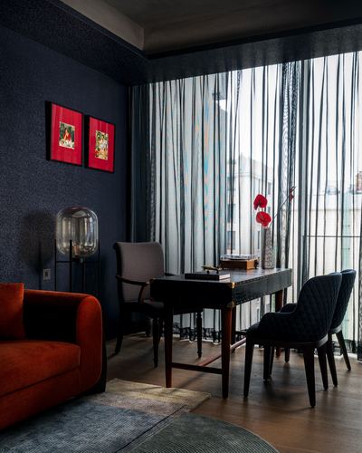 Dark navy living room corner with rust velvet sofa, dark writing desk, chairs, and sheer curtained window