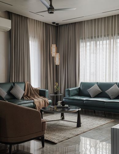 Living room with green leather sofas, round dark coffee table, and floor-to-ceiling curtained windows