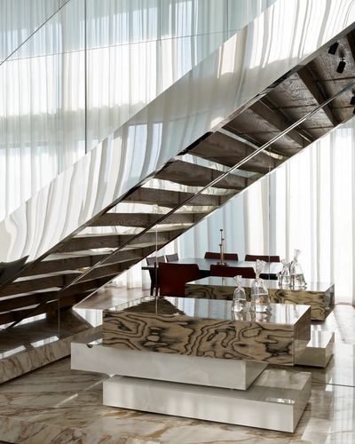 Floating staircase with mirrored soffit above a marble-topped dining console in a sunlit Dubai duplex