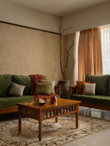 Living room corner with two green velvet sofas, carved wood coffee table, and patterned wallpaper wall
