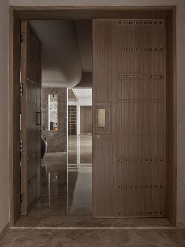 Large wood-grain door with brass stud grid opens onto a stone-floored hallway with a curved ceiling.
