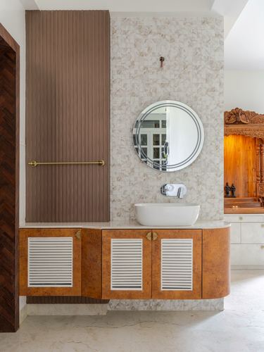 Bathroom vanity with round mirror, mosaic stone wall, and curved burl-wood cabinet with louvered doors