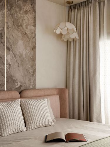 Bedroom corner with pink upholstered headboard, stone accent wall, and scalloped pendant light