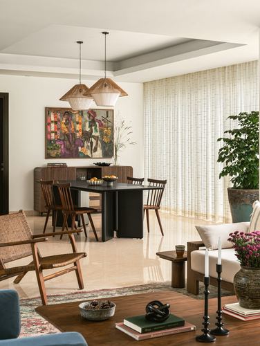 Open living-dining space with black dining table, spindle chairs, woven pendants, and sheer curtained window