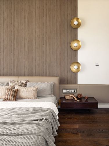 Bedroom with wood-panelled wall, three brass disc sconces, upholstered bed and dark wood nightstand