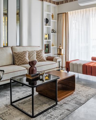 Living room with cream sofa, wood-and-glass coffee table, and built-in display niches by sheer curtained window