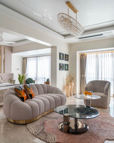 Beige living room with tufted sofa, layered marble tables, and crystal chandelier under natural light