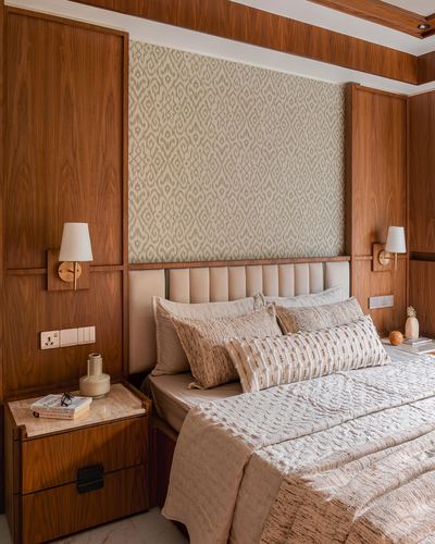 Wood-paneled bedroom with upholstered headboard, patterned wallpaper panel, brass sconces, and marble-top nightstand