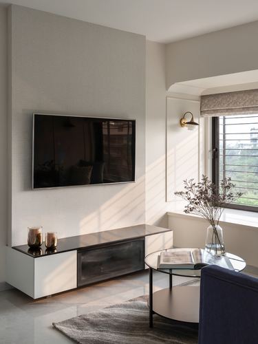 Living room with tv on textured wall, glass coffee table, sunlit window with roman blind