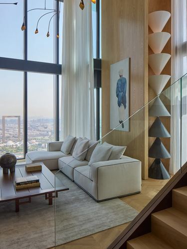 Double-height living room with cream sectional, oak paneling, and stacked cone lights beside a staircase
