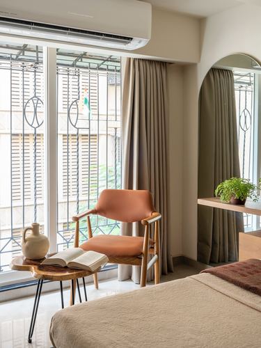 Bedroom corner with tan leather armchair by window, arched mirror niche, terracotta bedcover