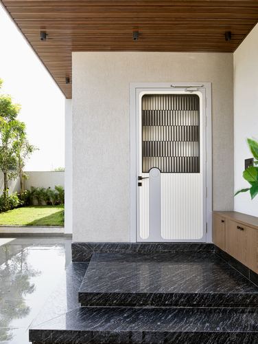 Entrance porch with wood-slat ceiling, grey textured wall, white ribbed door, black stone steps