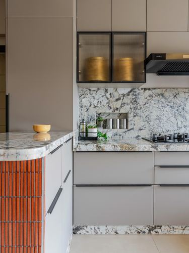 Modern kitchen with veined stone backsplash, black fluted cabinet doors, and a curved orange-tiled island edge