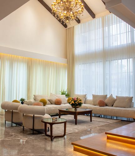 Double-height living room with chandelier, sheer curtains, cream sectional and marble flooring