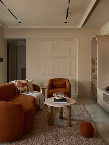 Terracotta velvet sofa and armchair in a lime-plastered living room with a sculptural wall relief