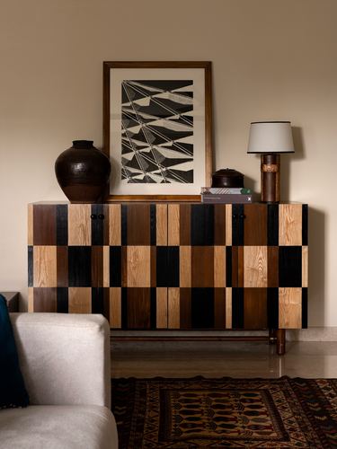 Checkered wood sideboard with framed art, vase and lamp against beige wall