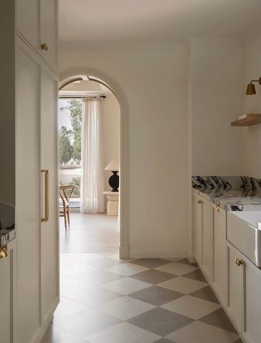 Cream kitchen with arched doorway, marble counter, checkerboard floor and brass hardware