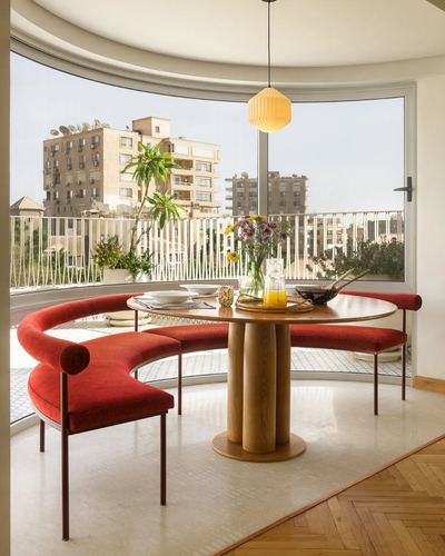 Curved red velvet banquette around round wood table by a bowed window overlooking Cairo rooftops