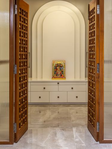 Open jaali wooden doors reveal an arched pooja niche with a small deity frame on a cabinet