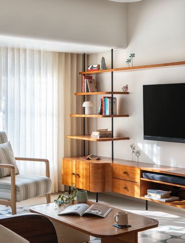 Sunlit living room corner with wood shelving unit, tv, striped armchair and terrazzo-pattern rug