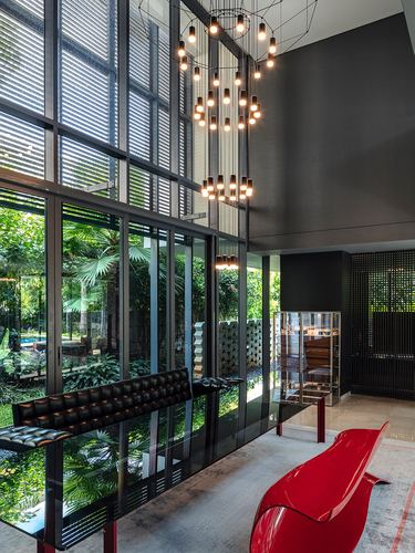 Double-height living space with glass facade, cluster pendant lights, tufted bench and red sculptural chair