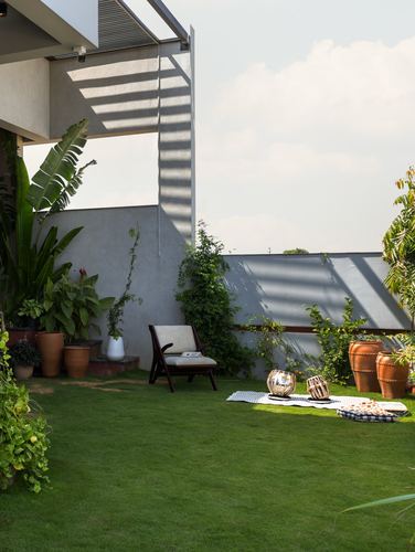 Terrace garden with lounge chair, terracotta pots, and tabla drums on grass under striped shadow