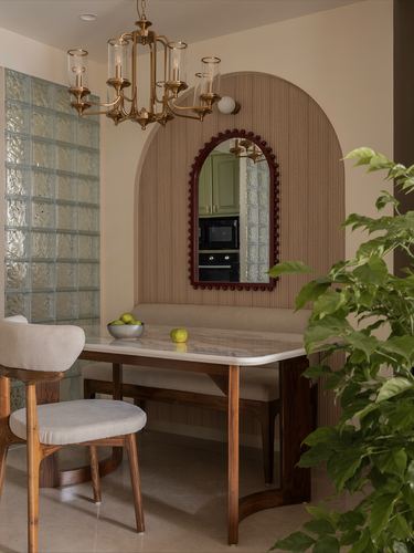 Dining nook with arched fluted wall, brass chandelier, wood table, and burgundy-framed mirror