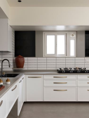 White L-shaped kitchen with ribbed tile backsplash, brass handles, and terracotta pot on counter