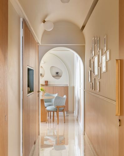 Arched hallway with wood paneling and gallery wall leading to dining area with blue chairs