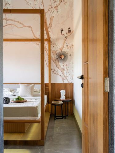 Wooden four-poster bed against floral bird wallpaper, seen through an open ribbed door