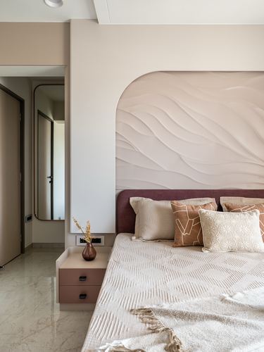 Bedroom with wave-textured plaster headboard wall, maroon upholstered bed, pink bedside table.