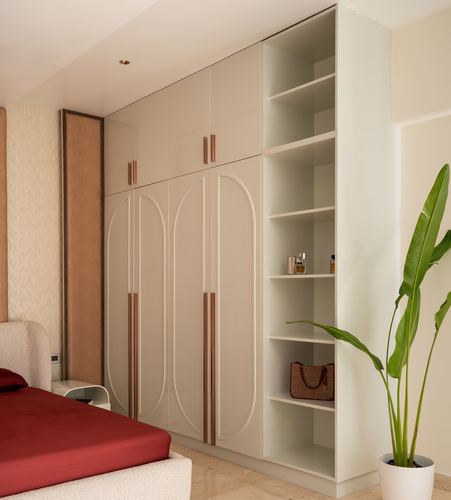 Beige wardrobe with oval fluted door panels and brass handles beside open shelving and a red bed