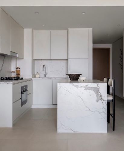 Minimalist kitchen with veined marble waterfall island, handleless cabinetry, and black bar stools