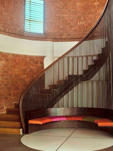 Curved brick staircase with wooden slat railing above a round built-in bench with colorful cushions