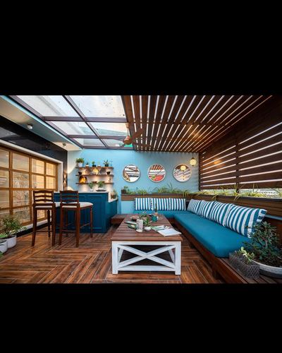 Covered terrace lounge with teal built-in seating, striped cushions, wooden slatted ceiling and round wall mirrors