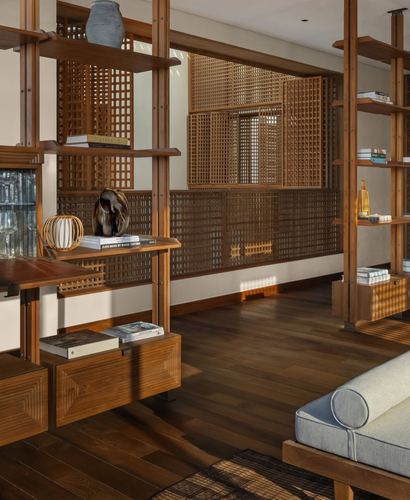 Wood shelving unit and lattice screen wall in a warmly lit living space with dark wood flooring