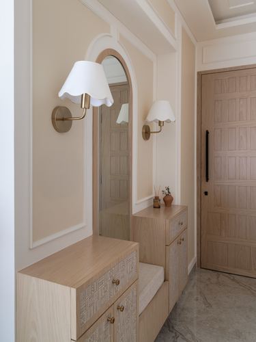 Beige foyer with arched mirror, brass sconces, wood console with drawers and paneled door