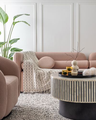 Pink boucle sofa and armchair around a black and white striped inlay coffee table in a paneled living room