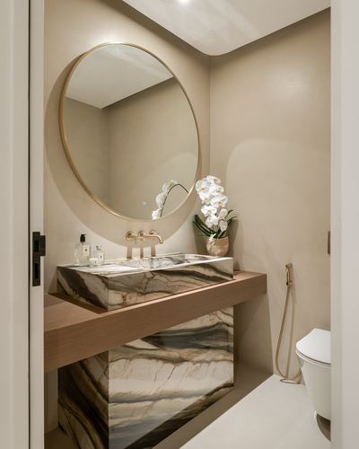 Powder room with round brass mirror above a veined stone vanity and wood shelf, orchid beside faucet