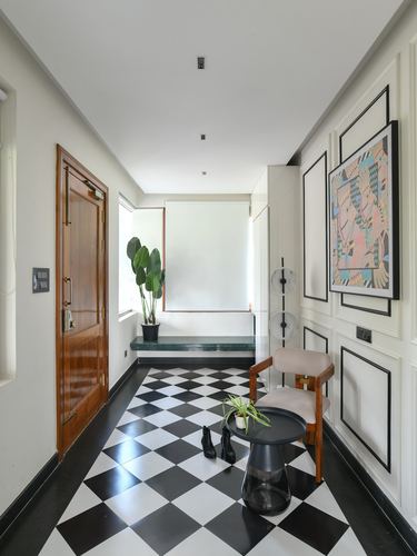 Black and white checkerboard foyer with wooden door, panelled wall, framed art, and cane chair