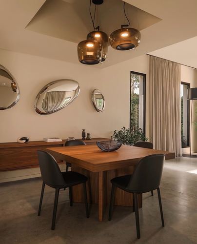 Dining room with square wood table, black chairs, brass pendant lights, and asymmetric mirrors above a walnut sideboard