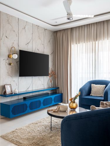Living room with marble-look wall, wall-mounted TV, blue fluted console, and blue velvet armchairs