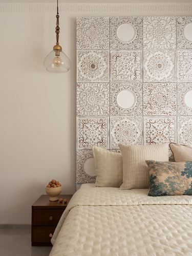 Bed against a carved mandala-tile headboard wall with a brass pendant light beside it